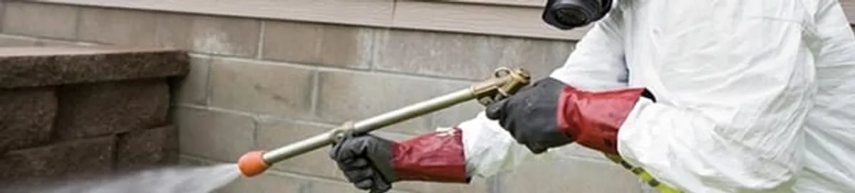 Pest control technician applying exterior insect treatment along a home foundation in Columbia, MO