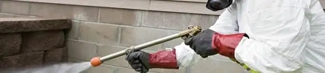 Pest control technician applying exterior insect treatment along a home foundation in Columbia, MO