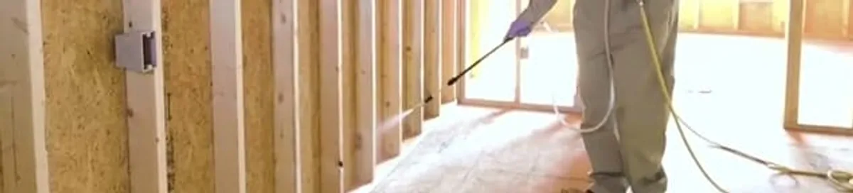 Termite treatment technician applying spray along framing and unfinished walls in Columbia, MO