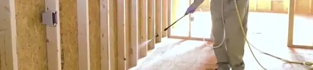 Termite treatment technician applying spray along framing and unfinished walls in Columbia, MO